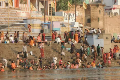 Tłum ludzi w barwnych strojach kąpie się i odpoczywa na schodach nad rzeką Ganges.