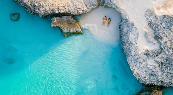 Para na plaży na wyspie Aruba, relaksująca się w turkusowej wodzie i na białym piasku, otoczona skalistymi klifami.
