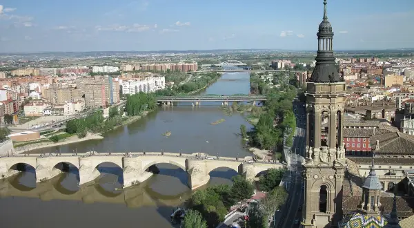 Widok na rzekę Ebro w Saragossie, z kamiennym mostem i wieżą bazyliki w tle.