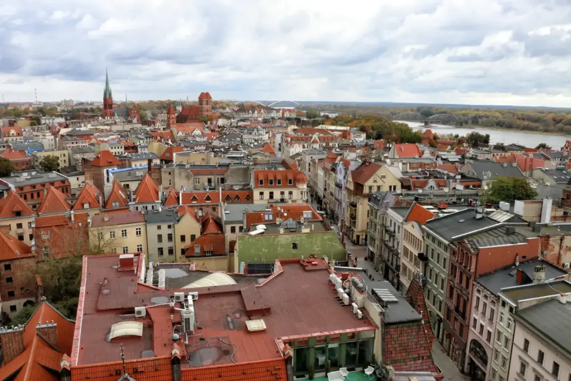 Widok na **Toruń stare miasto** z lotu ptaka. Czerwone dachy kamienic, kościelne wieże i Wisła w tle.