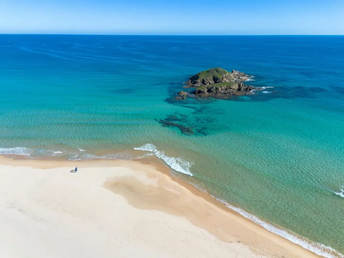 Pusta plaża na Costa Smeralda, z turkusową wodą i samotną postacią spacerującą brzegiem.