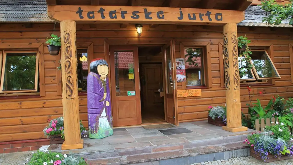 Drewniana fasada z napisem "tatarska jurta". Przed wejściem stoi kolorowa rzeźba postaci w stroju tatarskim.