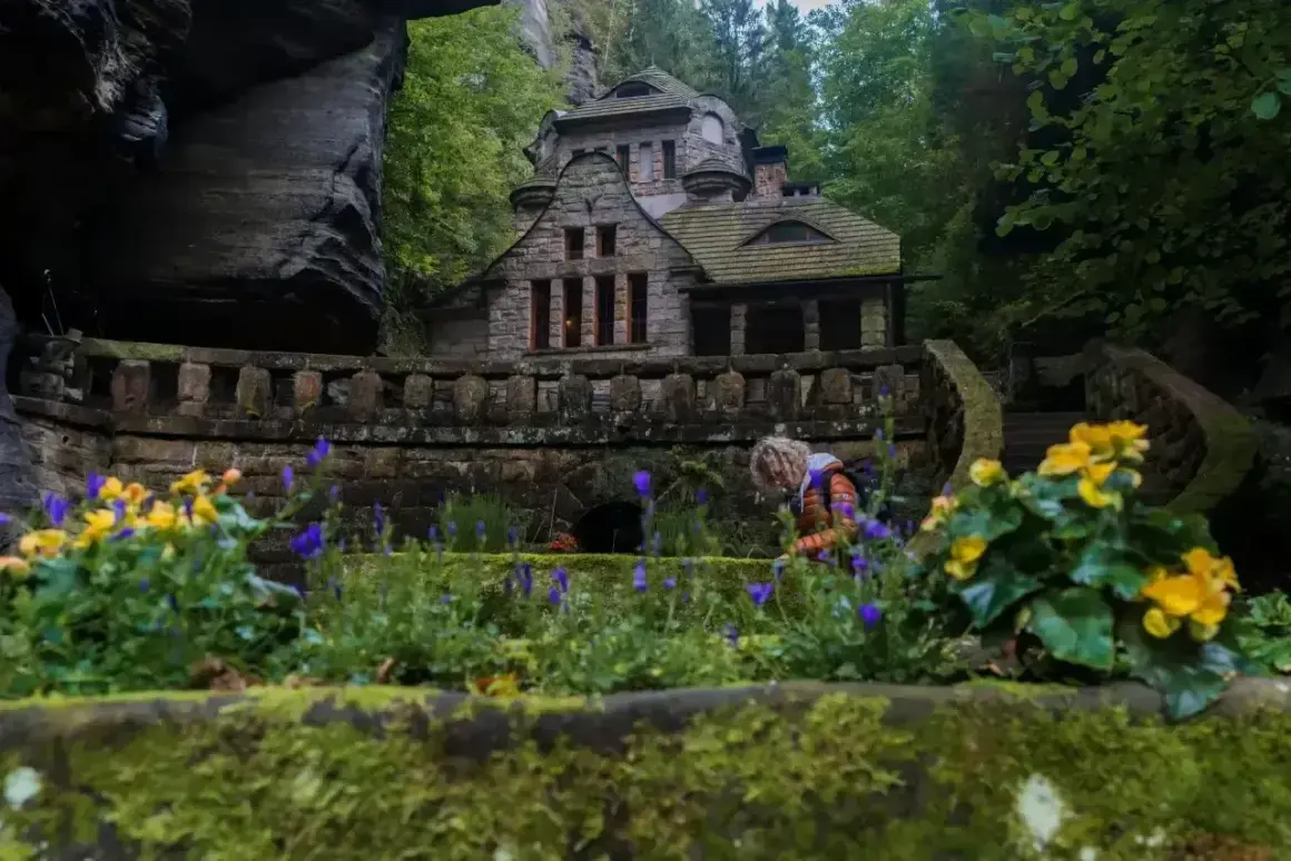 Kamienny domek w skalnym otoczeniu, idealne miejsce na czeska szwajcaria noclegi. Kwitnące kwiaty dodają uroku.