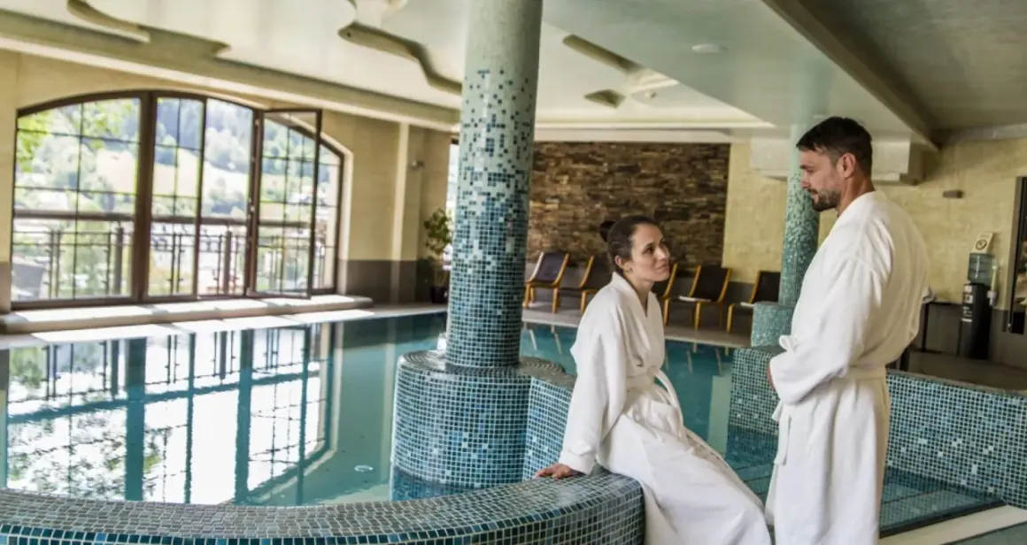 Para relaksu w Hotel Elbrus Spa & Wellness. Para w szlafrokach przy basenie, z widokiem na góry.