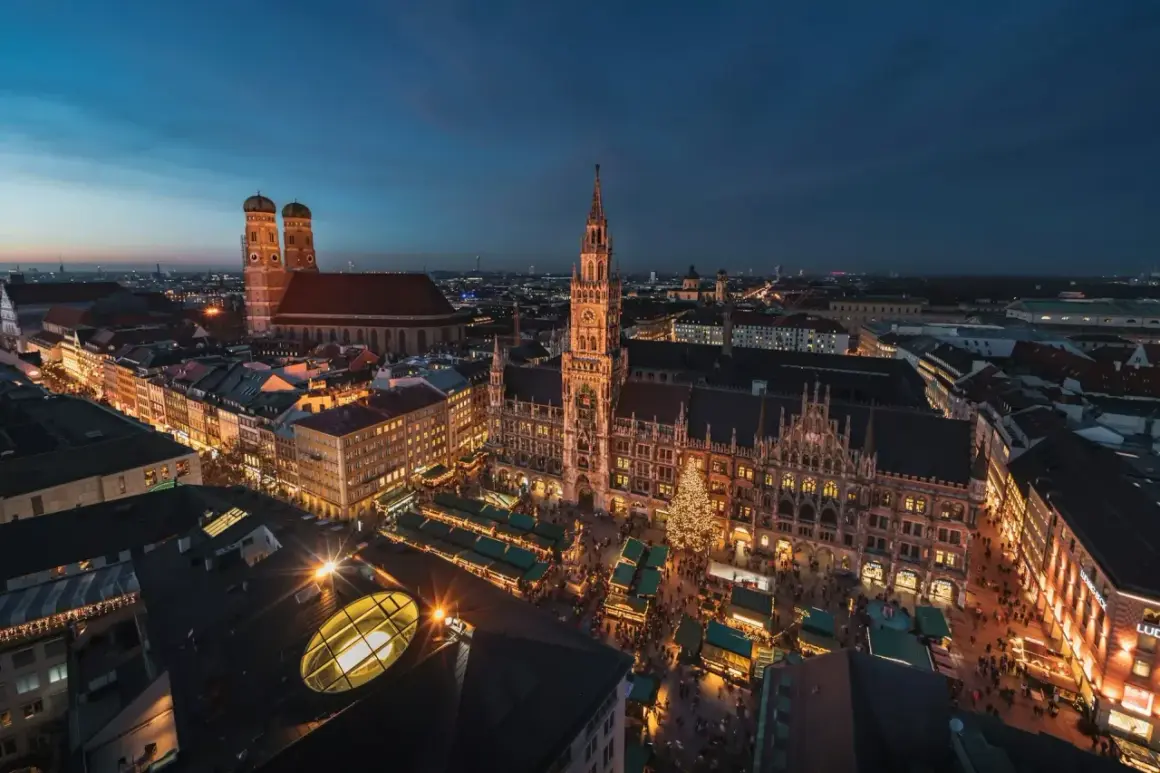 Nocny jarmark bożonarodzeniowy w Monachium. Rynek z oświetlonymi straganami i choinką, w tle majestatyczny Nowy Ratusz i katedra Frauenkirche.