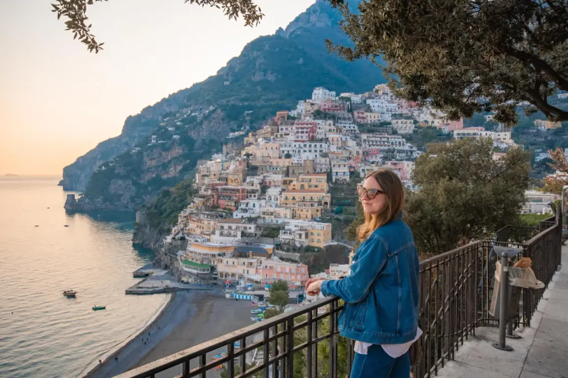 Kobieta podziwia malownicze miasta we Włoszech, Positano, z widokiem na morze i kolorowe domy wznoszące się po zboczu góry.