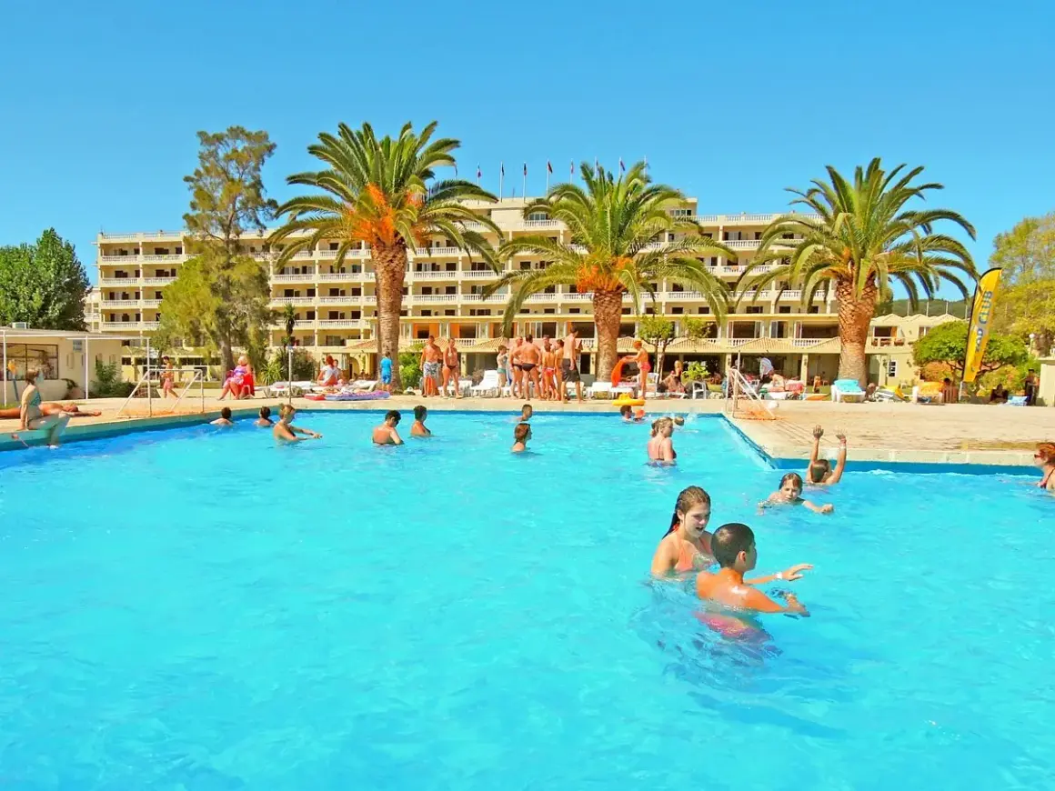 Słoneczny dzień na basenie w Messonghi Beach Holiday Resort. Rodziny kąpią się i bawią w wodzie.