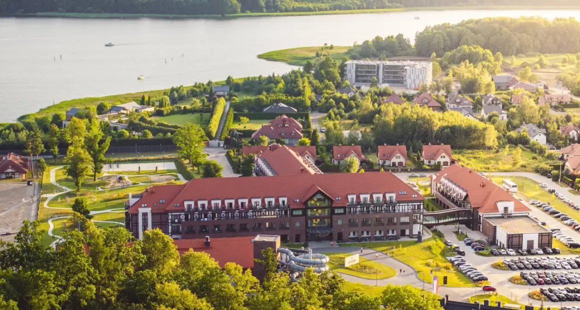 Widok z lotu ptaka na kompleks hotelowy Radisson z czerwonymi dachami, otoczony zielenią i jeziorem.