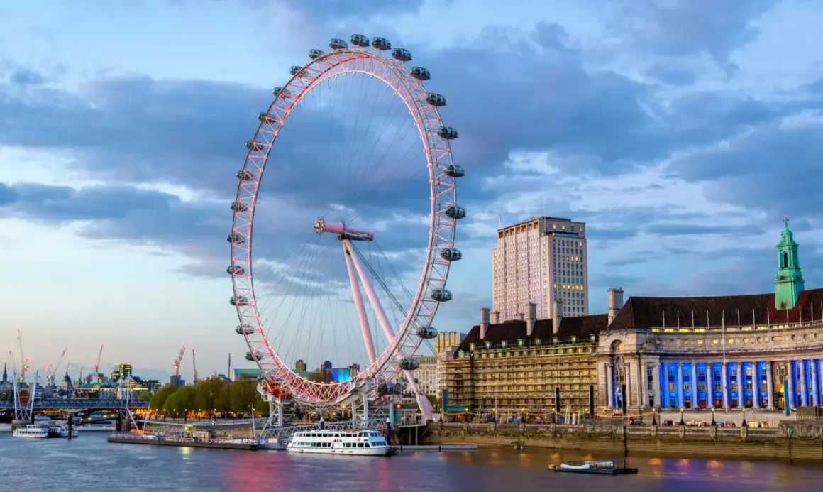 London Eye oświetlone wieczorem, z widokiem na Tamizę i budynki w tle.