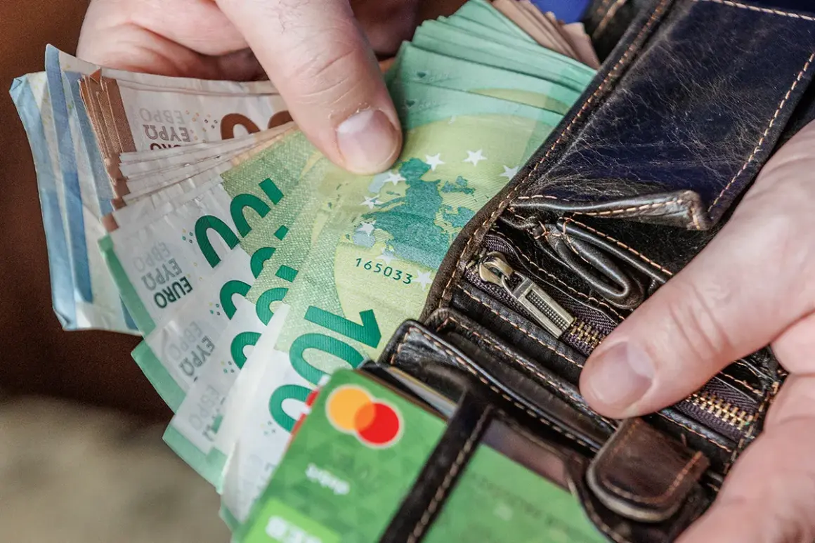 Ręce trzymają portfel z banknotami euro. Widać też kartę debetową. Litwa używa euro jako swojej waluty.