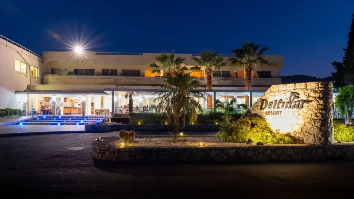 Nocny widok na Delfinia Resort. Podświetlone schody prowadzą do wejścia. Kamienny znak z nazwą hotelu.