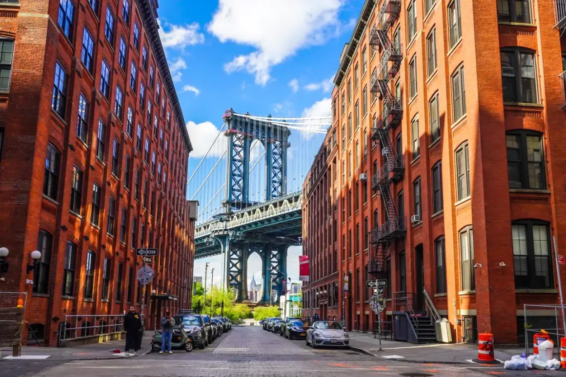 Urokliwe dzielnice Nowego Jorku: Manhattan Bridge wyłaniający się między ceglanymi kamienicami z DUMBO.