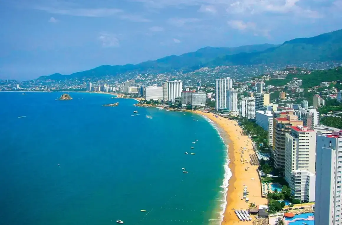 Słoneczna plaża w Acapulco z turkusową wodą, białymi hotelami i zielonymi wzgórzami w tle.
