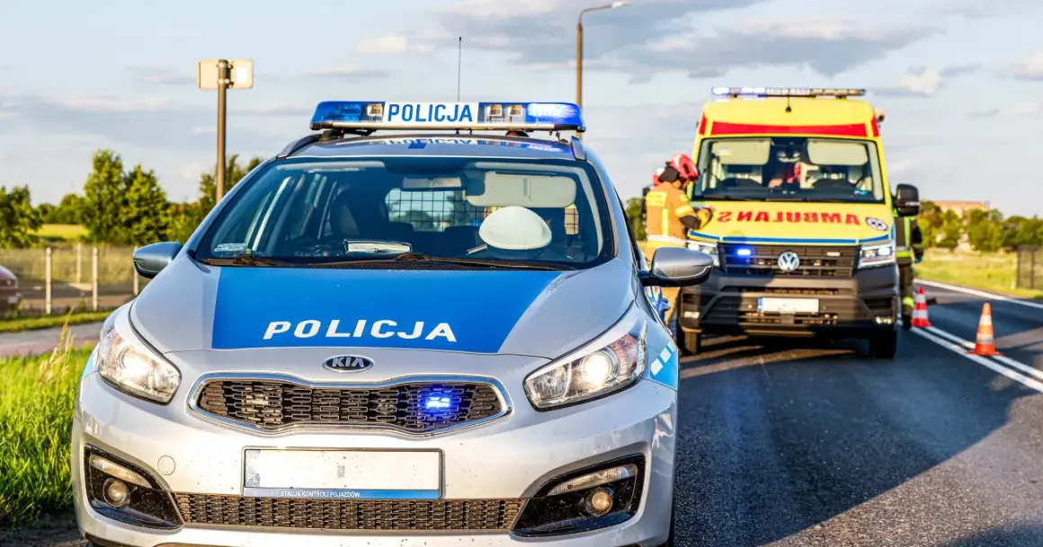 Radiowóz policyjny i karetka na poboczu drogi w Emilianowie. Służby zabezpieczają miejsce zdarzenia.