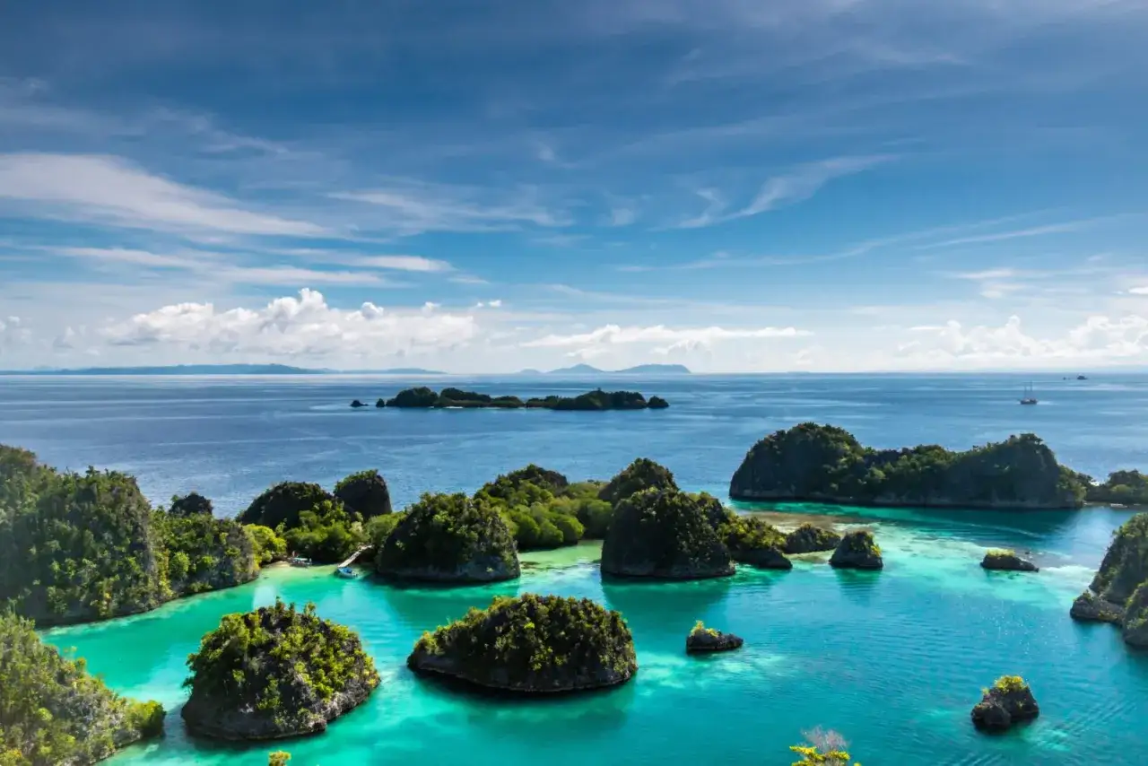 Rajskie krajobrazy Raja Ampat: turkusowa woda, bujna zieleń i skaliste wysepki pod błękitnym niebem.