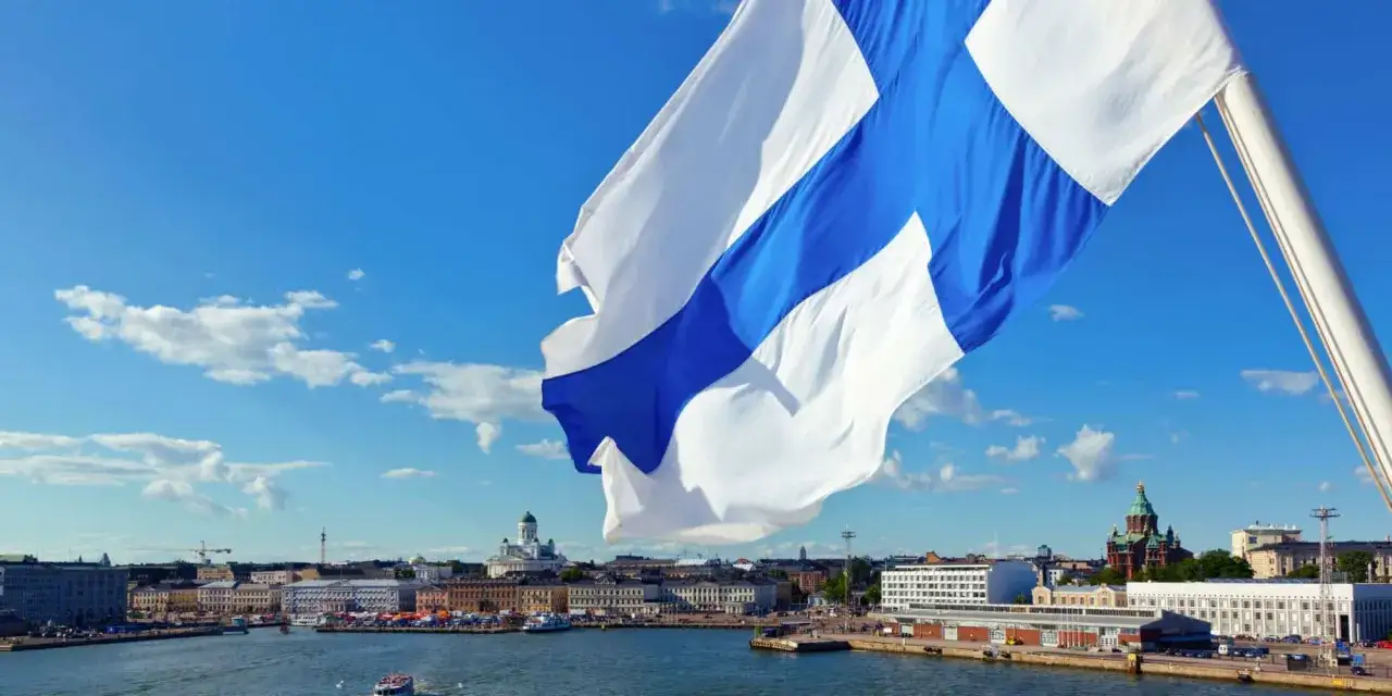 Flaga Finlandii powiewa nad Helsinkami. W tle widać port i charakterystyczne budynki, przypominające o tym, że Finlandia waluta to euro.
