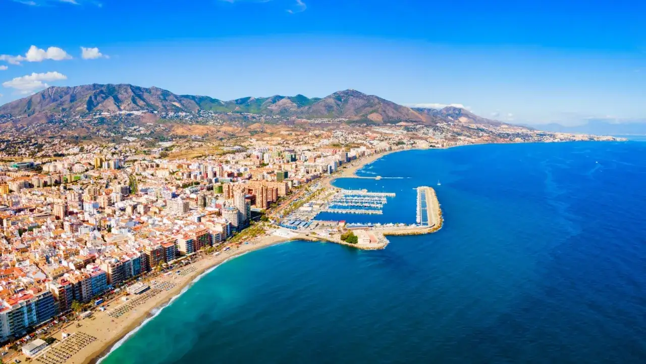 Widok na wybrzeże z górami w tle. Widać plażę, miasto i marinę. Tak właśnie wygląda miejsce, gdzie leży Malaga.