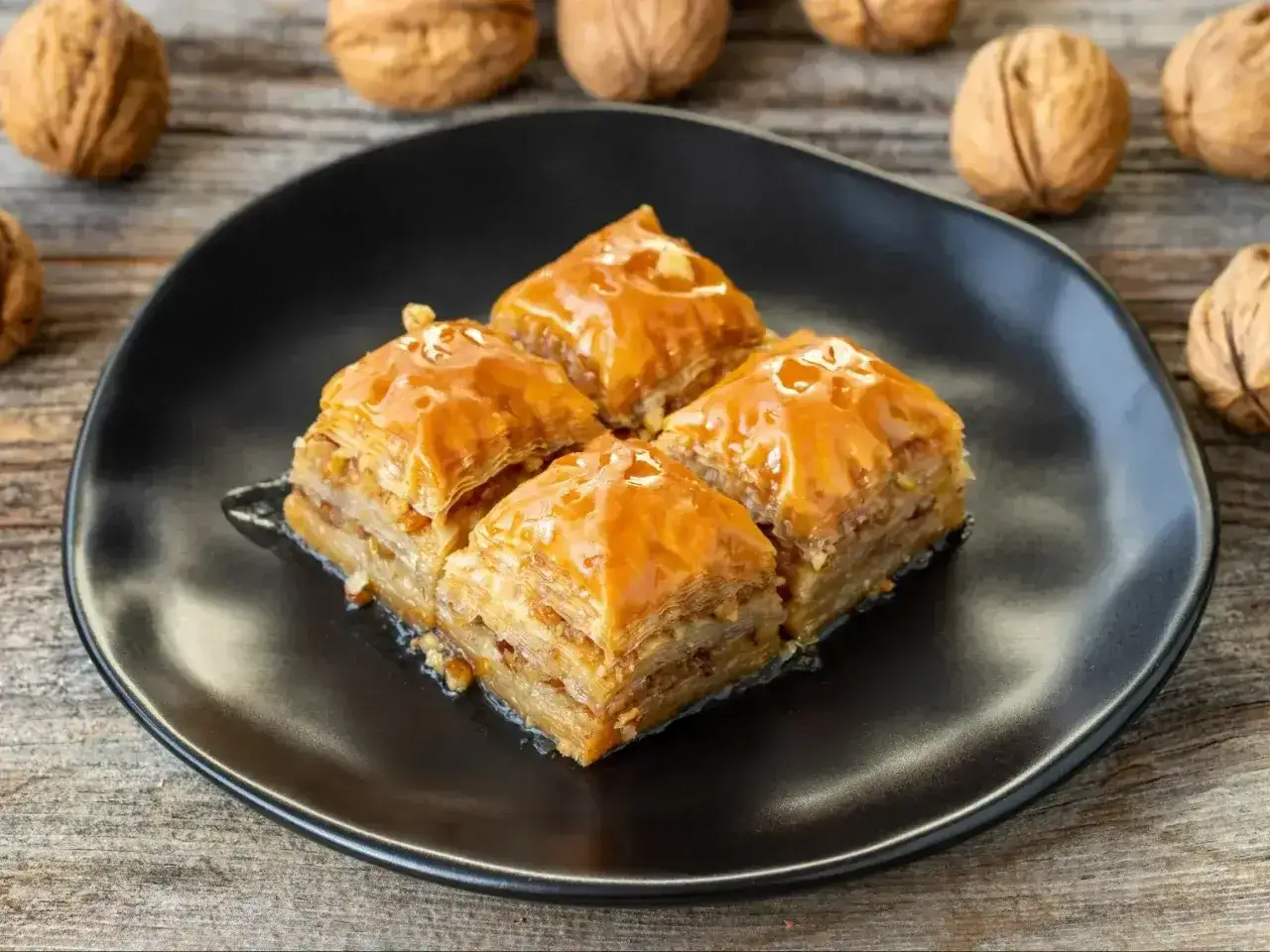 Cztery kawałki baklawy, słodkiego ciasta filo z orzechami, na czarnym talerzu. To jest właśnie baklava, co to za przysmak!