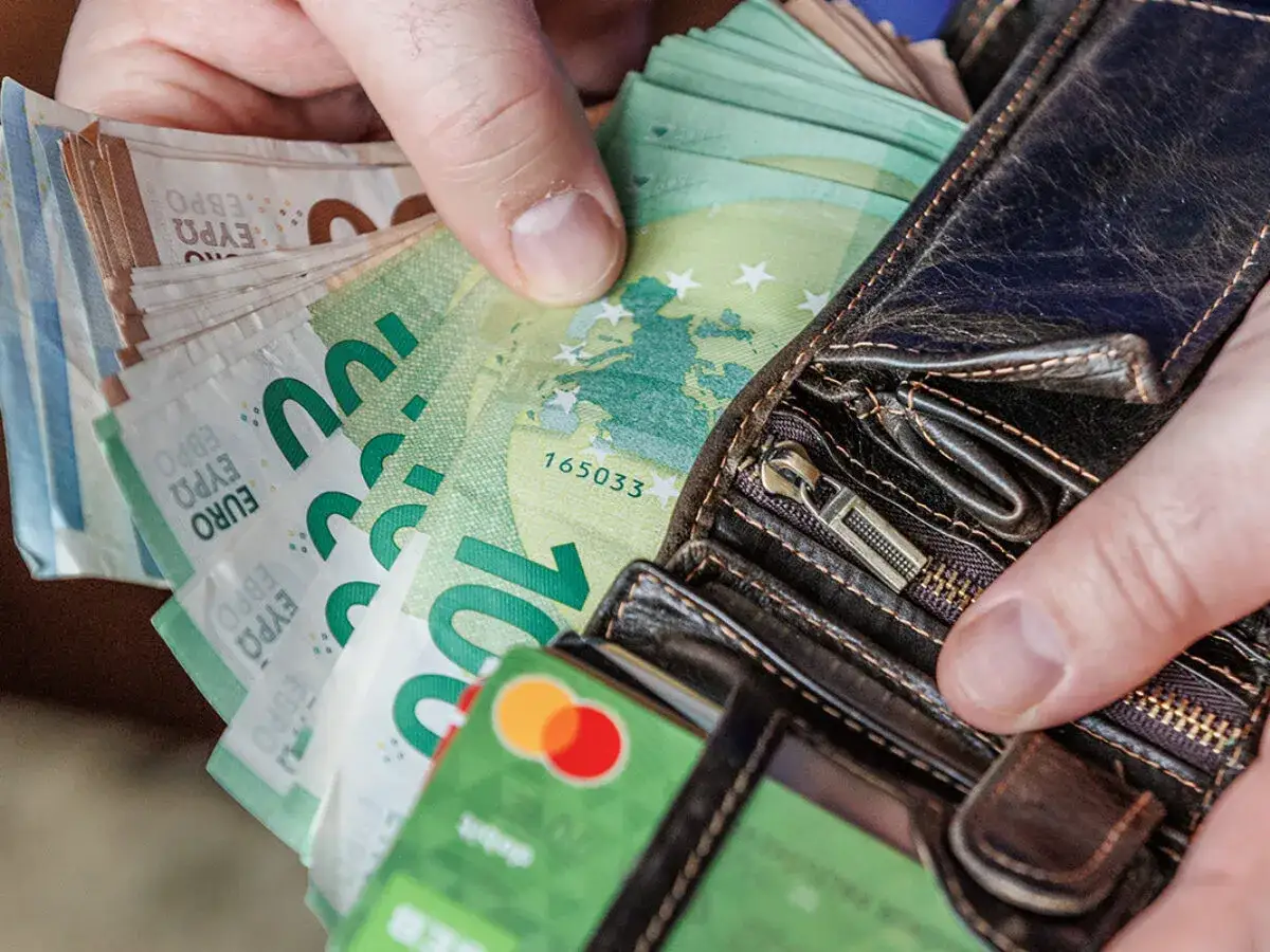 Ręce wkładają do portfela banknoty euro, w tym 100 euro. To nowa waluta Litwy, która niedawno dołączyła do strefy euro.