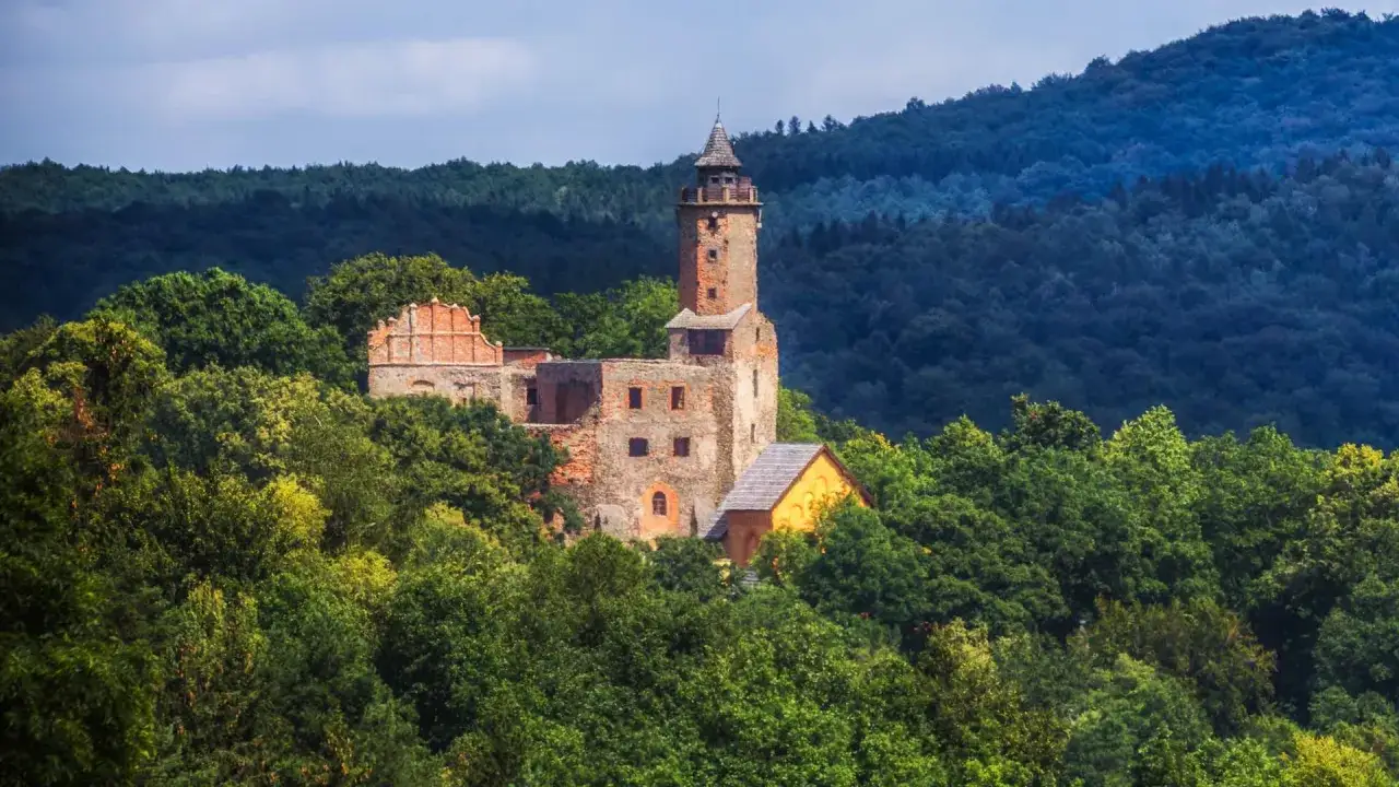 Ruiny zamku na wzgórzu otoczone lasem, w oddali widać jezioro Bystrzyckie.