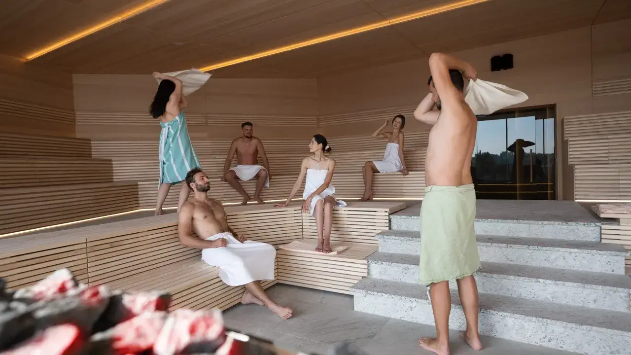 Relaks w saunie. Ludzie w ręcznikach odpoczywają na drewnianych ławach. Hotel Binkowski opinie potwierdzają wysoki standard.