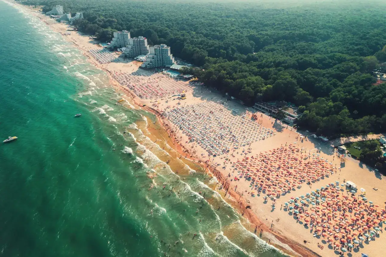 Słoneczne plaże Bułgarii pełne ludzi pod parasolami, turkusowe morze i zielony las. Idealne miejsce na wakacje.