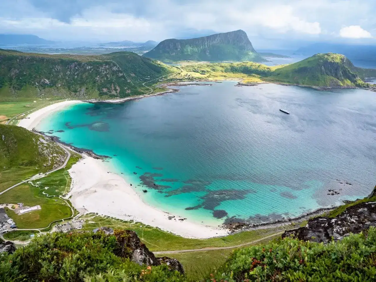 Widok z góry na zatokę z turkusową wodą i białą plażą na Lofotach. W oddali góry i samotny statek.