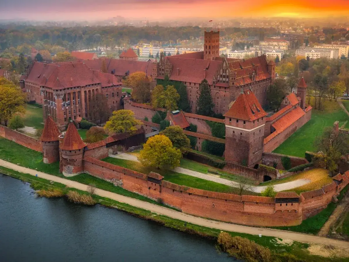 Malbork, największy zamek w Europie, w jesiennym słońcu. Potężne mury i wieże ceglanego kompleksu otaczają dziedzińce.