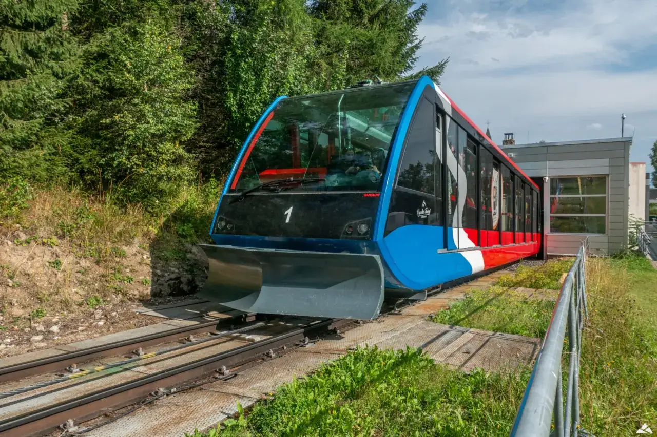 Nowoczesny stary smokowiec, kolej linowo-terenowa, wjeżdża na stację. Kolorowy wagon z niebieskim, białym i czerwonym pasem.