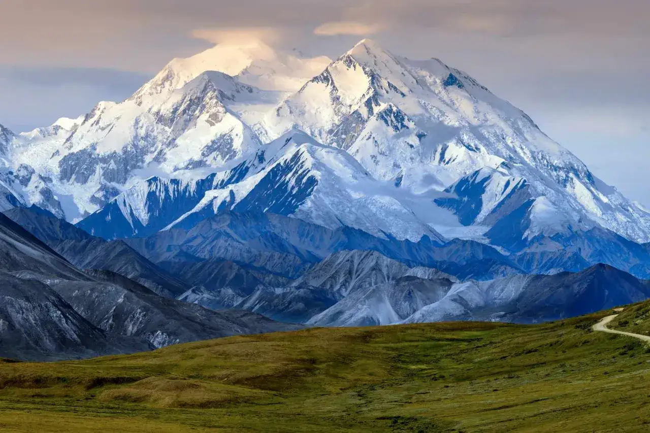 Majestatyczny, ośnieżony najwyższy szczyt Ameryki Północnej, Denali, góruje nad pasmami górskimi i zielonymi dolinami.