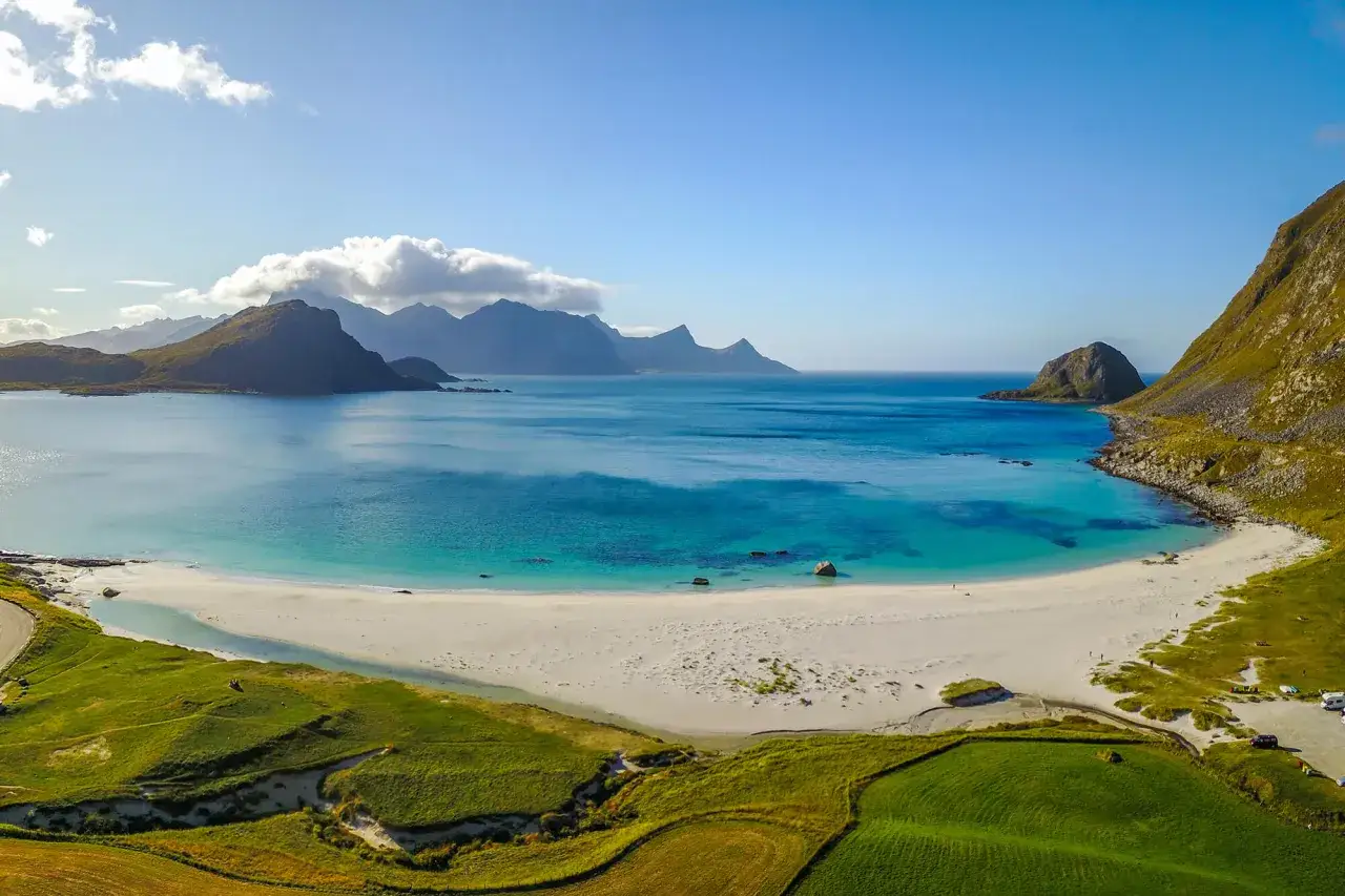 Malownicze fiordy norweskie z turkusową wodą, piaszczystą plażą i zielonymi wzgórzami.