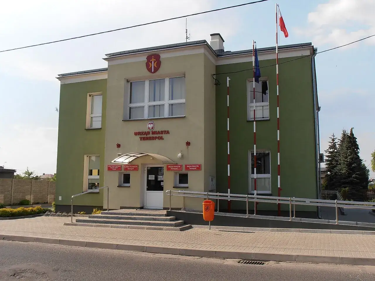 Urząd Miasta Terespol z polską i unijną flagą. Budynek ma zielono-żółtą elewację.
