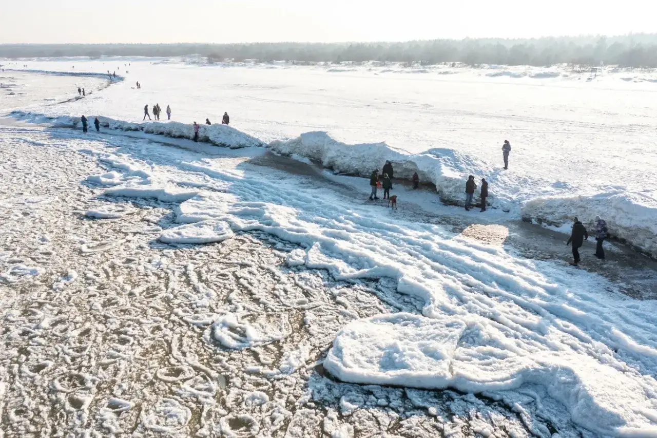 Mikoszewo zimą. Ludzie spacerują po zamarzniętym morzu, podziwiając lodowe góry i kry.