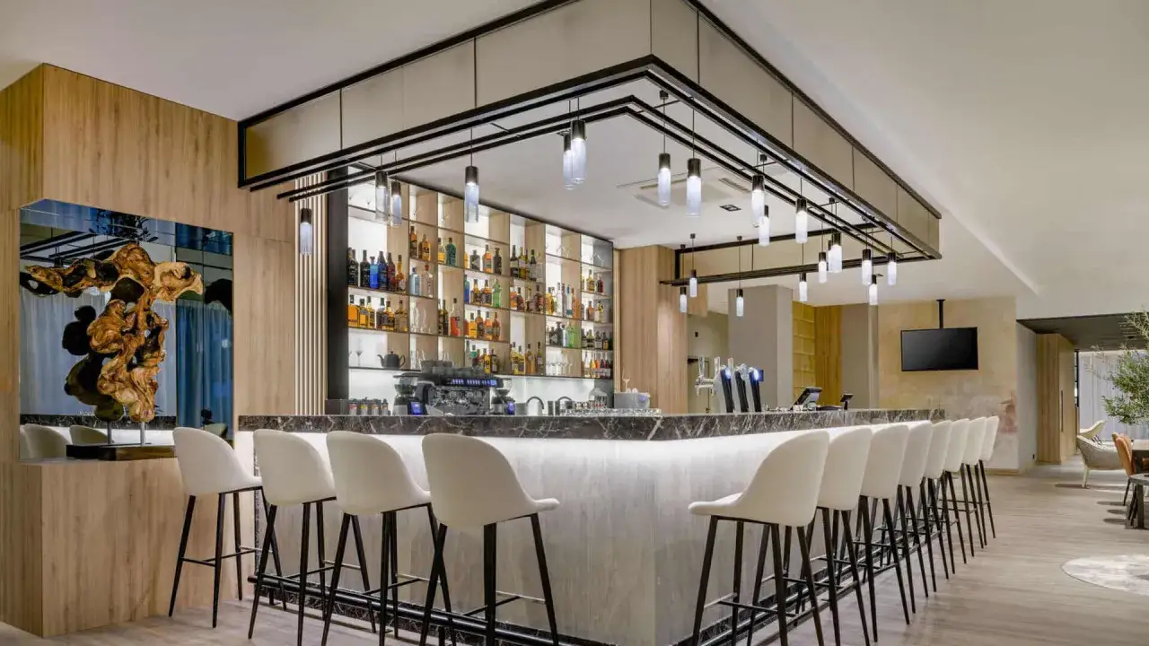 Nowoczesny bar w AC Hotels Krakow. Eleganckie krzesła barowe i bogato zaopatrzona półka z alkoholami tworzą idealne miejsce na relaks.