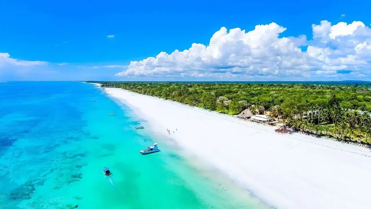 Rajska plaża Diani z turkusową wodą, białym piaskiem i łodziami. Tropikalna zieleń otacza wybrzeże.