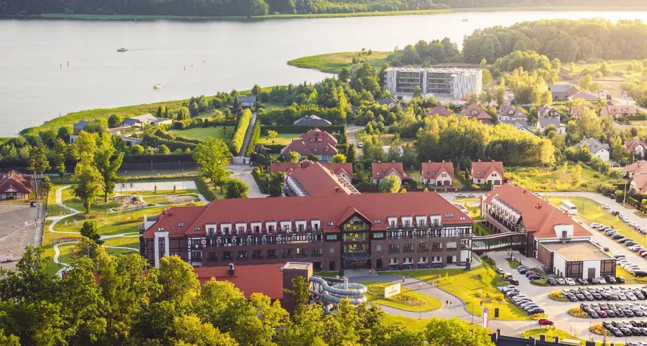 Widok na kompleks hotelowy Radisson z basenami i jeziorem w tle. Widać tu wiele budynków, parkingi i zielone tereny.