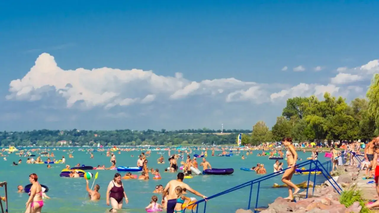 Tłum ludzi cieszy się latem na jeziorze Balaton. Woda jest pełna kąpiących się, pływających na materacach i bawiących się.