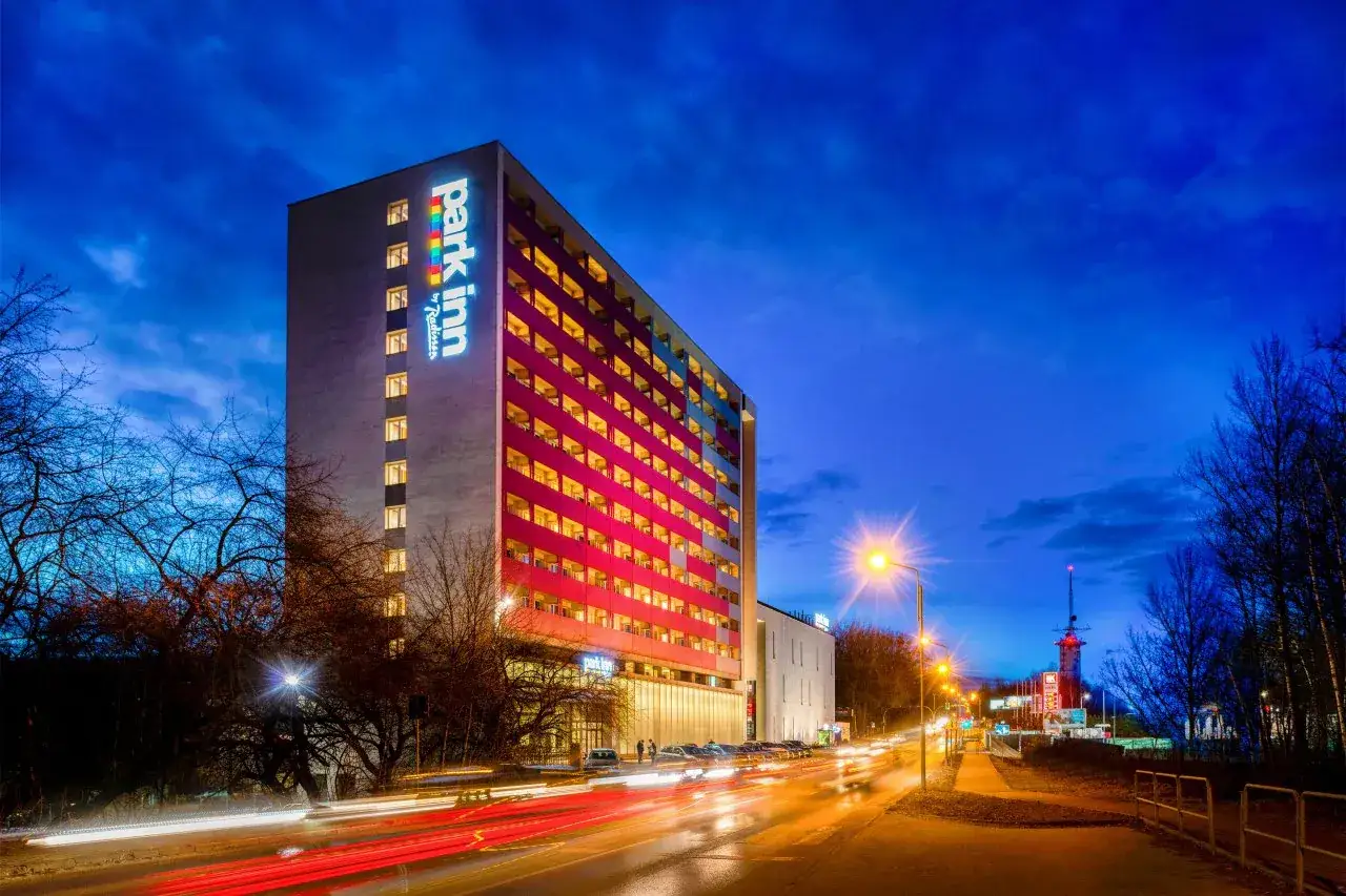 Wieczorna panorama miasta z oświetlonym budynkiem Park Inn Hotel Katowice i smugami świateł samochodów na drodze.