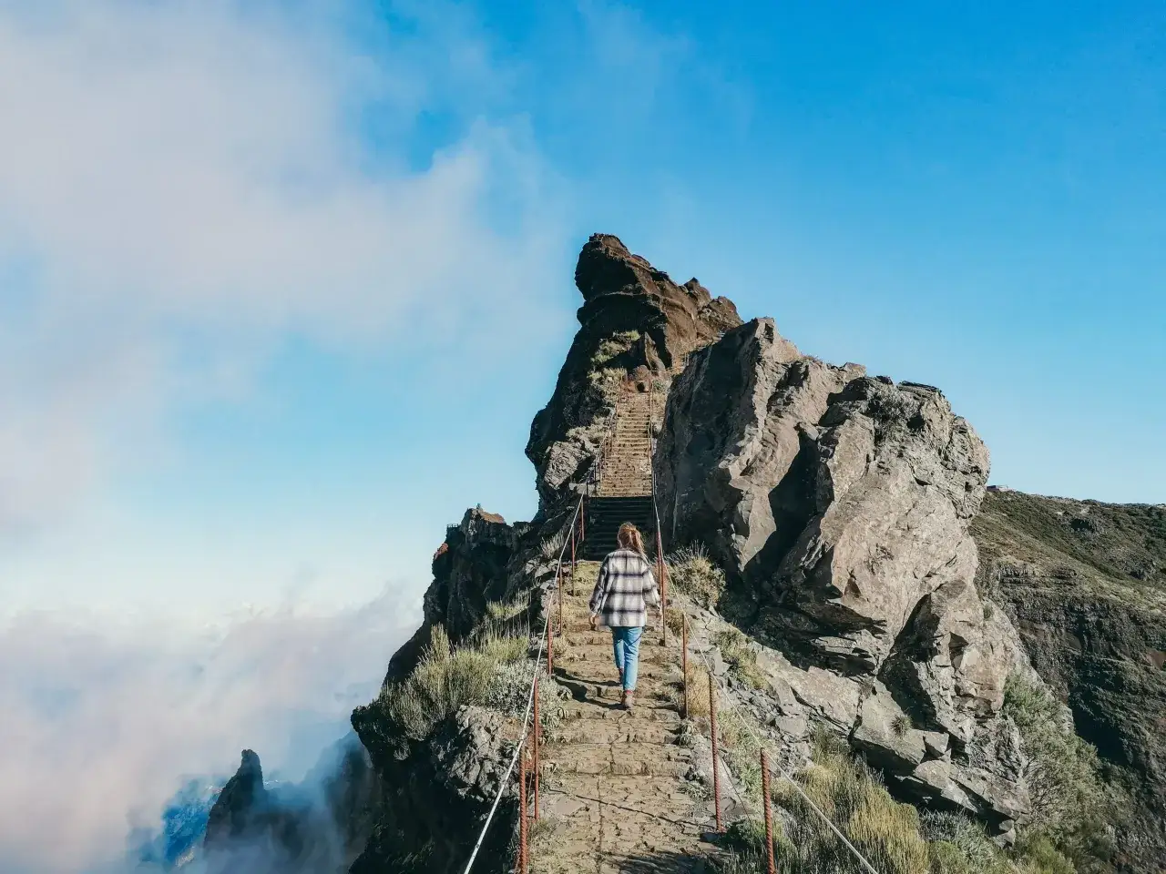 Droga na szczyt Pico do Arieiro, kamienne schody wiodące przez skaliste zbocza, chmury poniżej.