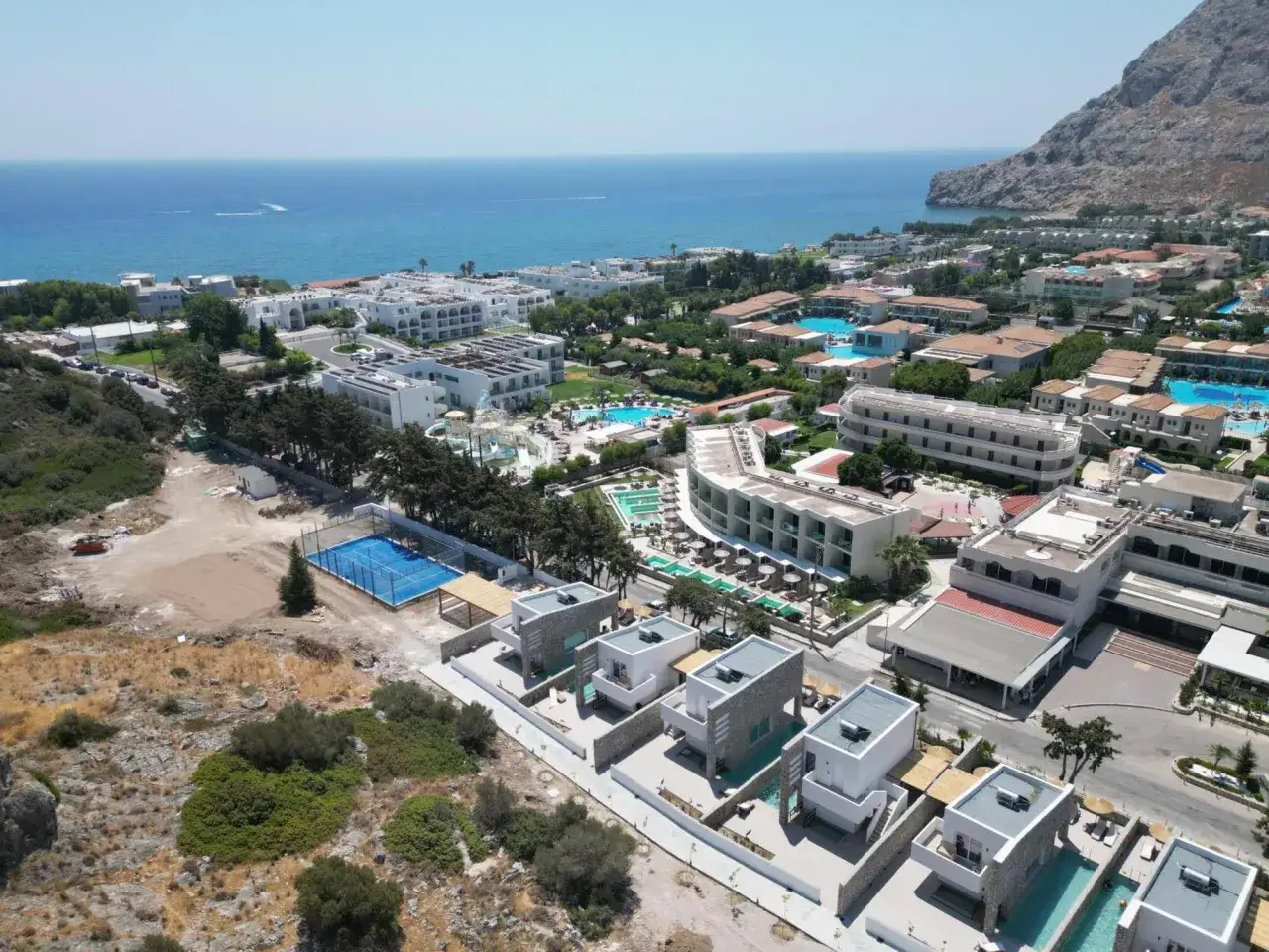 Widok na kompleks hotelowy Delfinia Resort z basenami i widokiem na morze. Wiele budynków, kort tenisowy i prywatne wille.