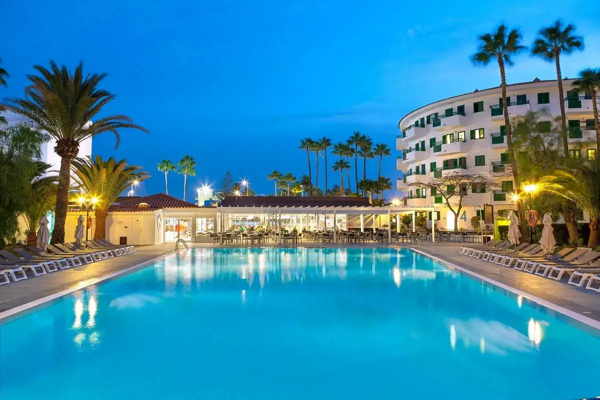 Basen hotelowy w Playa del Inglés o zmierzchu, z palmami i budynkiem hotelowym w tle.