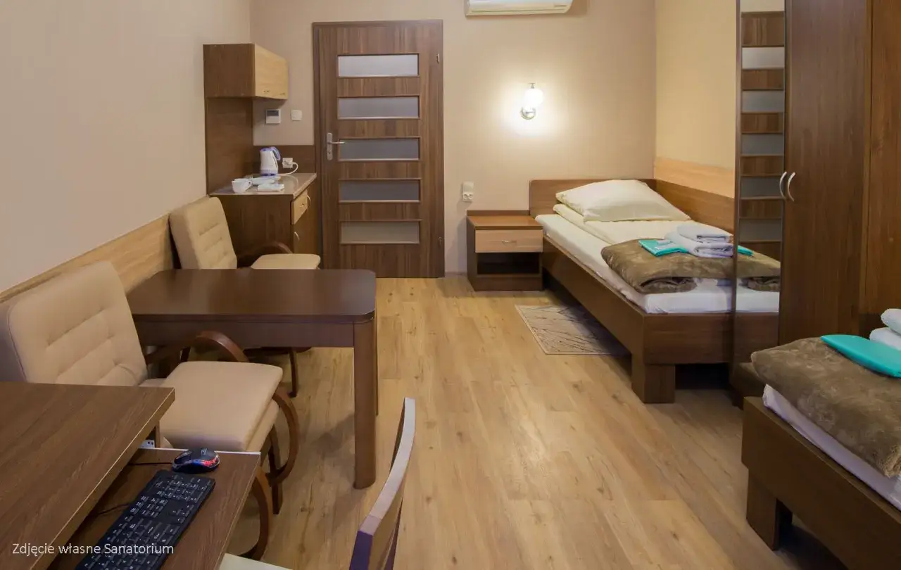 Pokój w sanatorium, łóżko, stół, krzesła, szafa. Czy to miejsce zasługuje na pozytywne sanatorium włókniarz opinie?