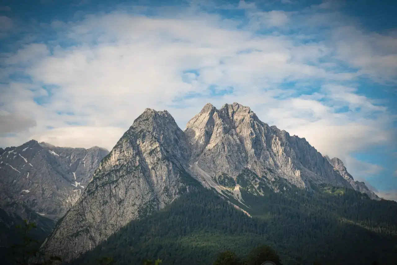 Majestatyczne szczyty Zugspitze, najwyższego szczytu Niemiec, wznoszą się na tle błękitnego nieba z chmurami.