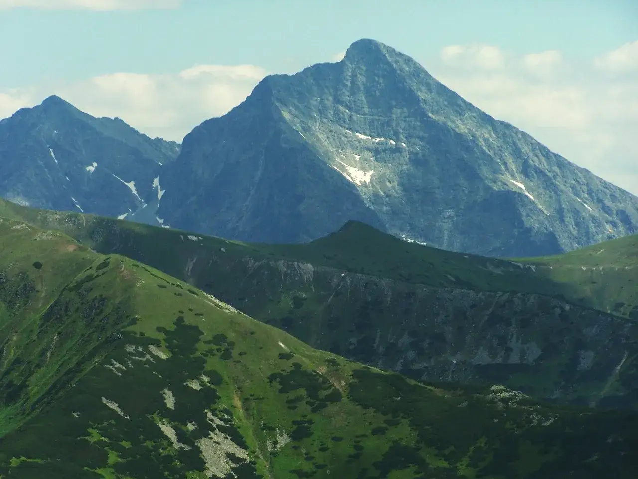Majestatyczny szczyt w Tatrach Wysokich 2494 m, otoczony zielonymi zboczami i skalistymi graniami, z resztkami śniegu.