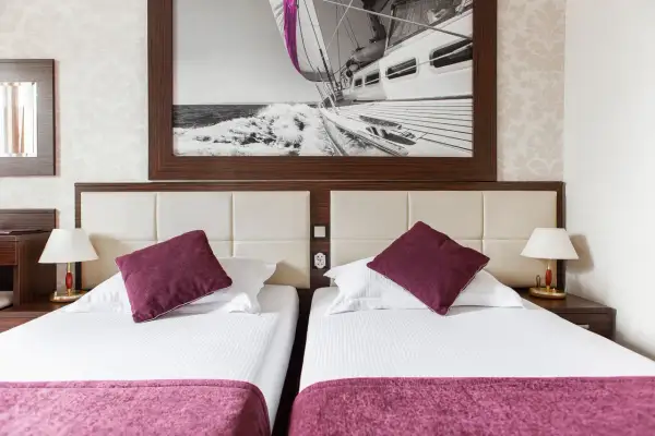 Dwie wygodne łóżka w pokoju hotelowym, nad nimi obraz z żaglówką. Idealne miejsce na wypoczynek, jak sugerują primavera jastrzębia góra opinie.