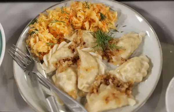 Pyszne pierogi z cebulką i koperkiem, podane z surówką z kiszonej kapusty. Idealne na mandu menu.