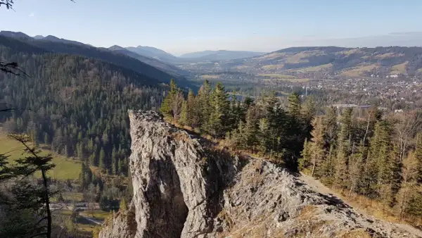 Widok z Nosala, góry samobójców, na Tatry i Zakopane. Skalisty szczyt, las i dolina.