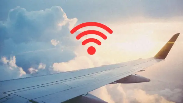 Widok z okna samolotu na chmury i skrzydło. Czerwony symbol Wi-Fi unosi się w powietrzu, sugerując, czy w samolocie jest wifi.