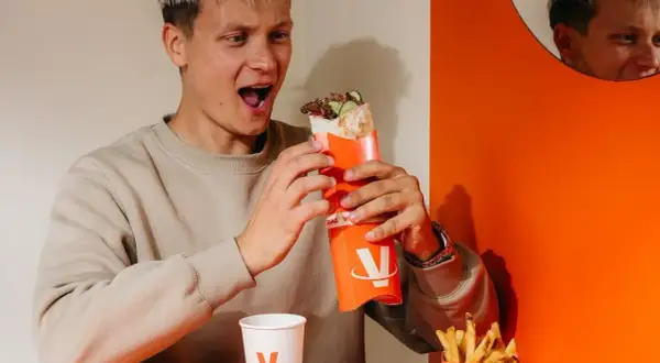 Młody mężczyzna z zachwytem trzyma w rękach viral kebab. Jego mina sugeruje, że opinie o tym daniu są w pełni uzasadnione.