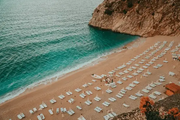 Plaża w Turcji, turkusowe morze, piaszczysty brzeg z rzędami leżaków i parasoli, skaliste wybrzeże.